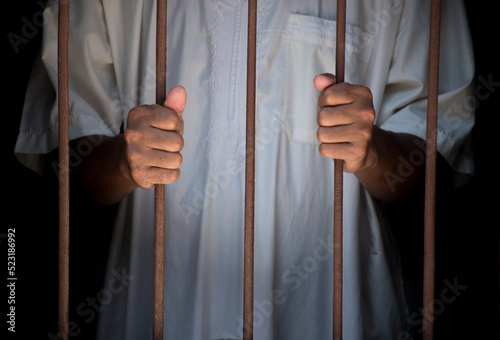 Religious muslim islam man in white session hold steel in jail on black background, concept for prisoner,sadness,detain,erroneousness © AfrandeePhotography