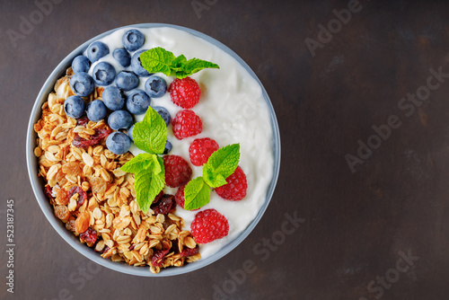 Granola with yogurt and berries on a dark brown background. Healthy breakfast with yogurt, baked granola, blueberries and raspberries. Top view. Copy space