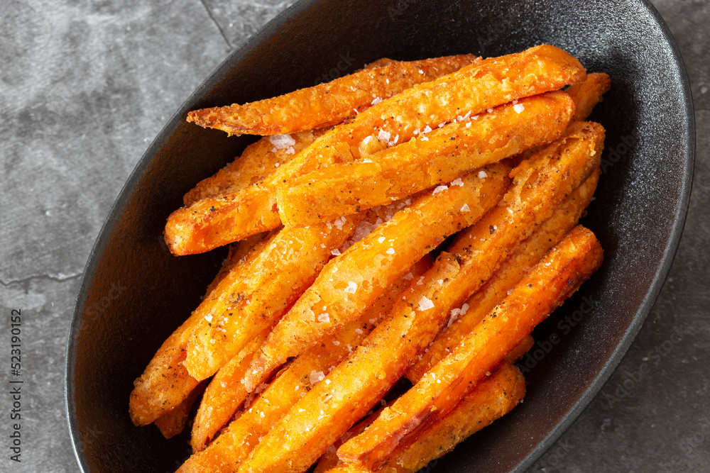 Sweet potato fries, seasoned with sea salt, in a black dish bowl. On a dark stone background Sweet potato fries, seasoned with sea salt, in a black dish bowl. On a dark stone background