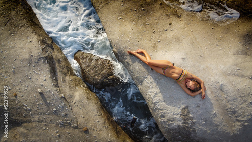 Woman in bikini relaxes on a rock