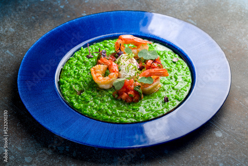 green risotto with shrimps, sliced tomatoes and cheese on blue plate