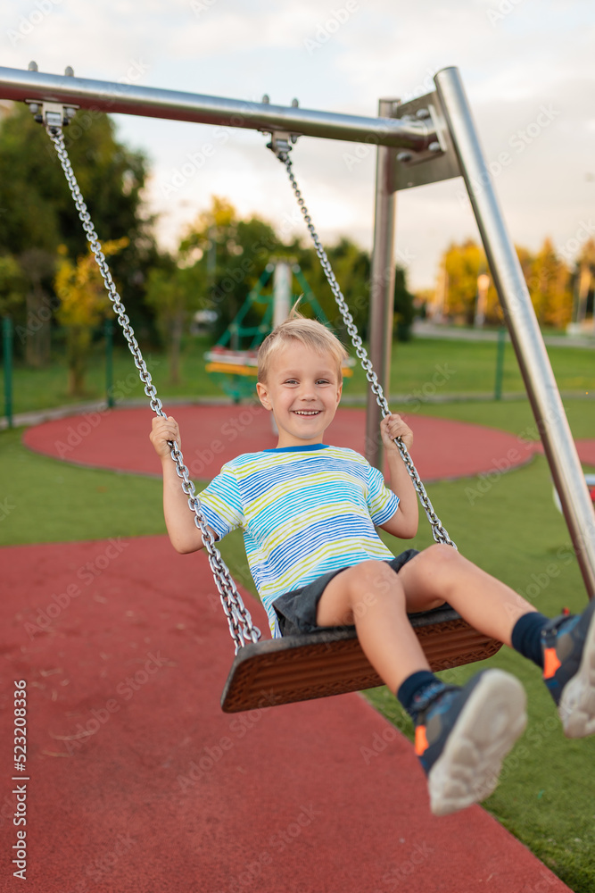 Active smiling boy on the swing and having fun. Happy children play in playground outside. Swinging uotdoor. Active smiling boy on the swing and having fun. Happy children play in playground outside. Swinging uotdoor.