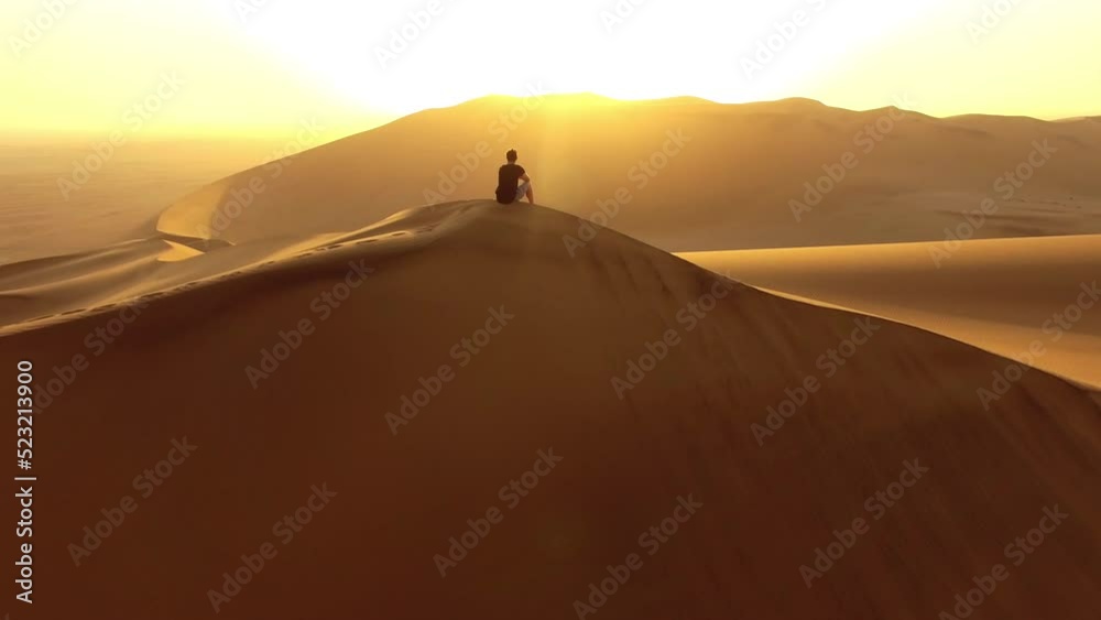Hiking, exploring and adventure with a young man sitting on a sand dune in a hot, arid and barren desert landscape. A hiker on a journey of discovery, traveling the world and seeing the sights