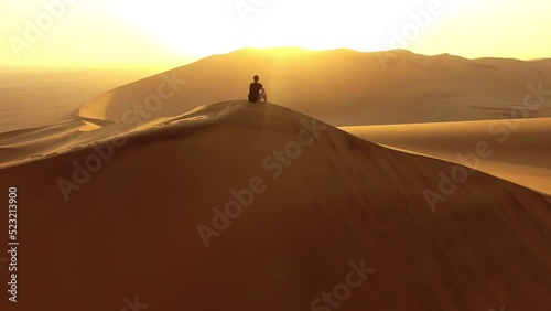 Hiking, exploring and adventure with a young man sitting on a sand dune in a hot, arid and barren desert landscape. A hiker on a journey of discovery, traveling the world and seeing the sights