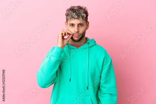 Young handsome caucasian man isolated on pink background showing a sign of silence gesture © luismolinero