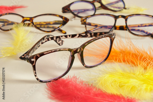 eyeglasses on beige background with colored feathers