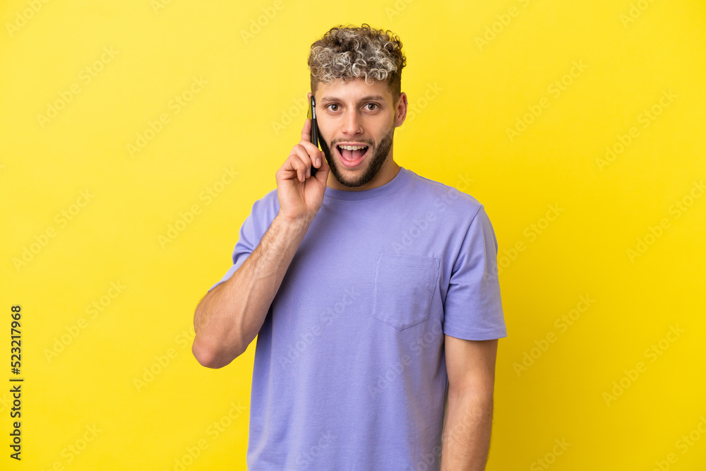 Fototapeta premium Young caucasian man using mobile phone isolated on yellow background with surprise facial expression