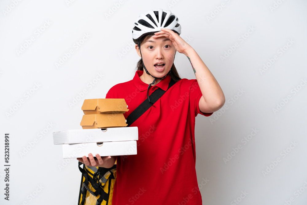 Young Chinese delivery woman taking takeaway food isolated on white background doing surprise gesture while looking to the side Young Chinese delivery woman taking takeaway food isolated on white background doing surprise gesture while looking to the side