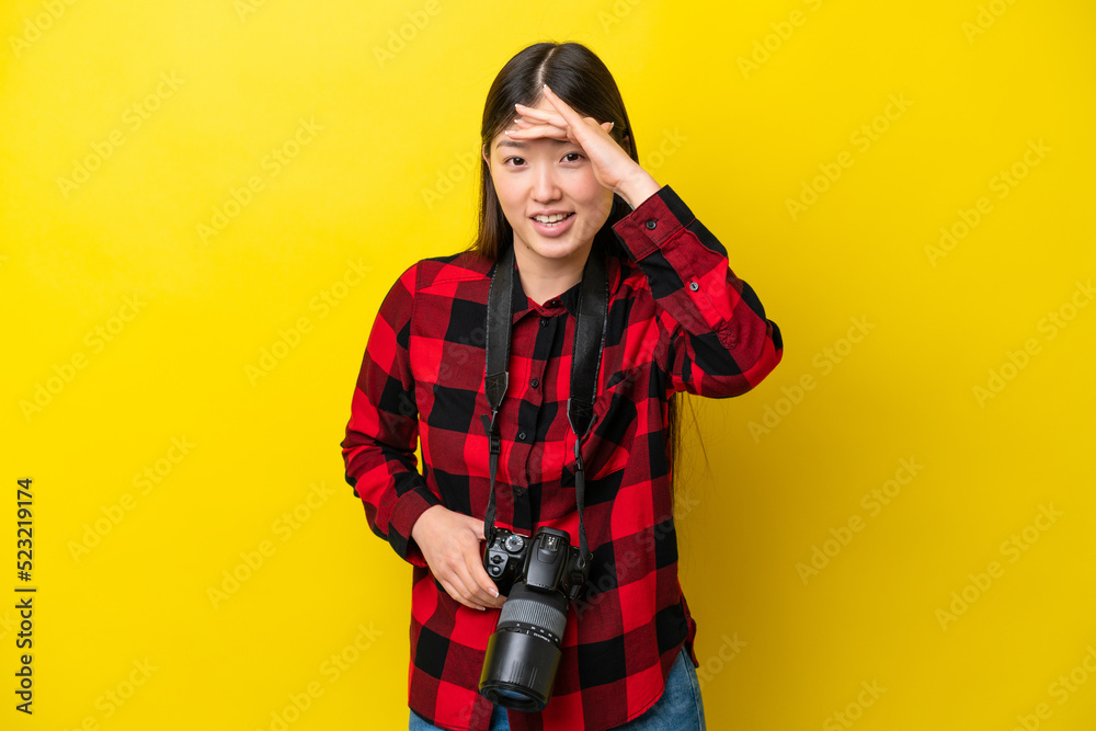 Young photographer Chinese woman isolated on yellow background looking far away with hand to look something Young photographer Chinese woman isolated on yellow background looking far away with hand to look something