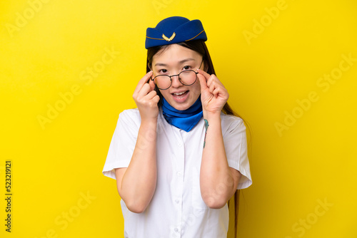 Airplane Chinese woman stewardess isolated on yellow background with glasses and surprised