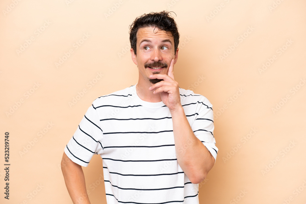 Young caucasian man isolated on beige background thinking an idea while looking up Young caucasian man isolated on beige background thinking an idea while looking up