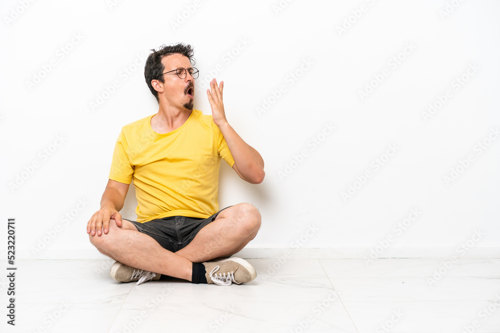 Young caucasian man sitting on the floor isolated on white background yawning and covering wide open mouth with hand Young caucasian man sitting on the floor isolated on white background yawning and covering wide open mouth with hand