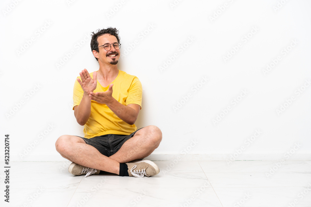 Young caucasian man sitting on the floor isolated on white background applauding after presentation in a conference Young caucasian man sitting on the floor isolated on white background applauding after presentation in a conference