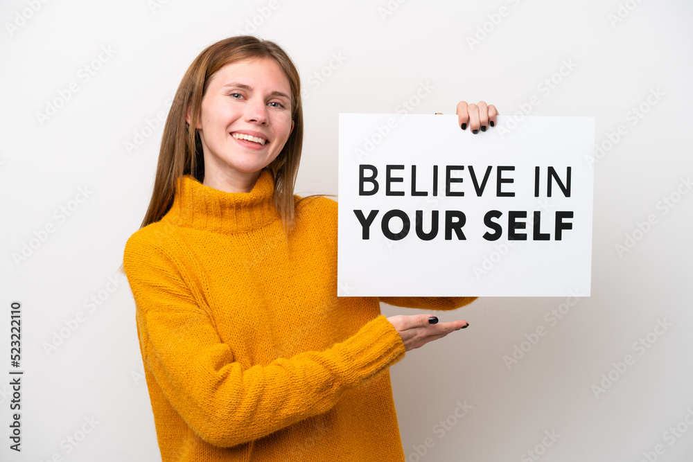 Young English woman isolated on white background holding a placard with text Believe In Your Self and pointing it Young English woman isolated on white background holding a placard with text Believe In Your Self and pointing it