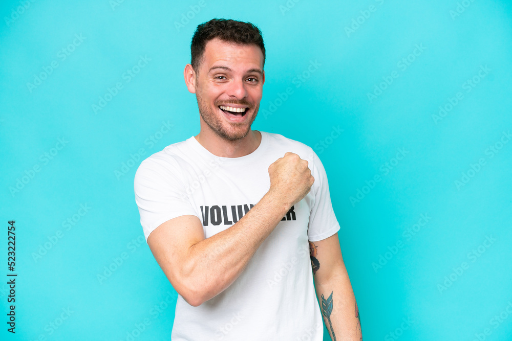 Fototapeta premium Young volunteer caucasian man isolated on blue background celebrating a victory