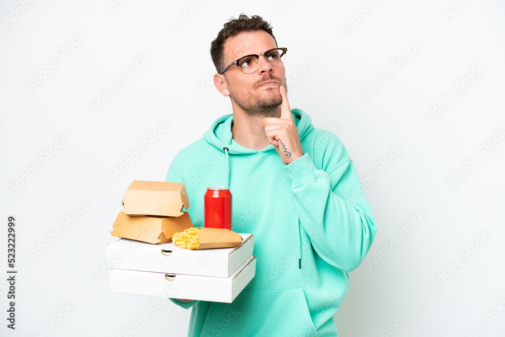 Young caucasian man holding fast food isolated on white background having doubts while looking up Young caucasian man holding fast food isolated on white background having doubts while looking up