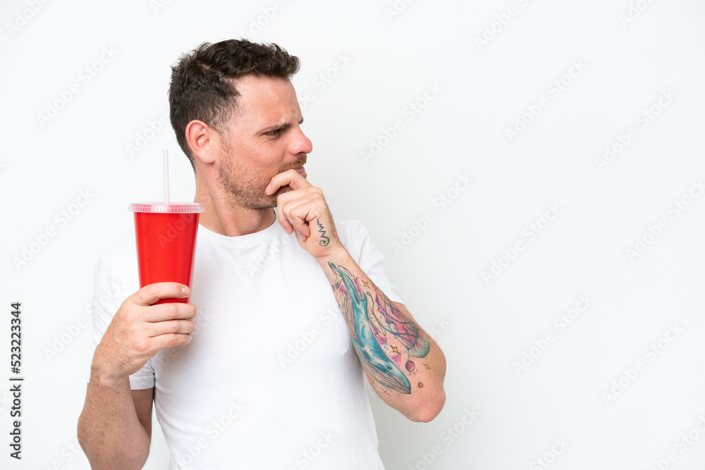 Young caucasian soda holding soda isolated on white background thinking an idea and looking side Young caucasian soda holding soda isolated on white background thinking an idea and looking side