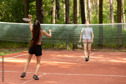 badminton tournament, teenager sport outdoor in the park in nature on a sunny summer day, two girls playing with badminton rackets in the park © yta