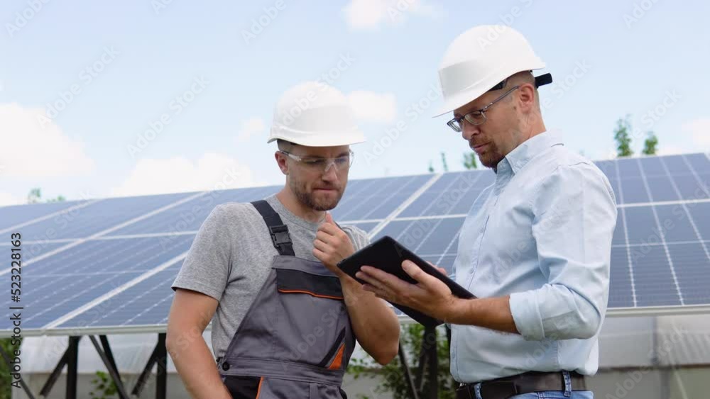 Two workers in helmets check the installed solar panels. Green electricity and alternative energy ecological concept Two workers in helmets check the installed solar panels. Green electricity and alternative energy ecological concept