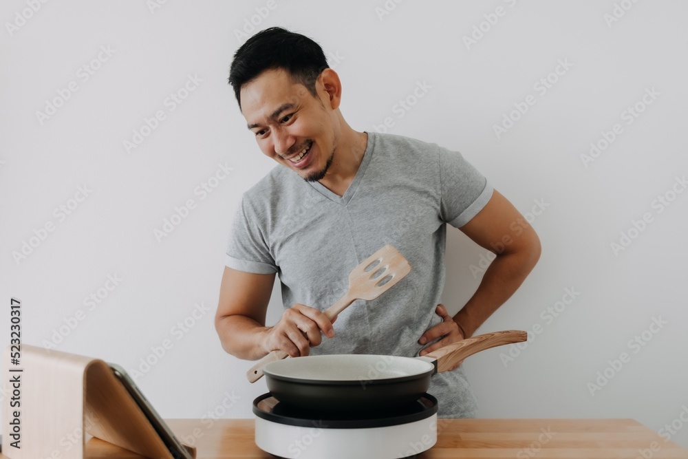 Happy asian man cooking online tutorial on tablet isolated on white background. Happy asian man cooking online tutorial on tablet isolated on white background.