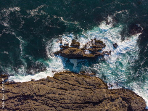 Top view of the raging ocean and rocky shore. A beautiful dark turquoise surface of the water and white foamy waves crash against the rocks on the shore. Ecology, beauty of nature. © Anton