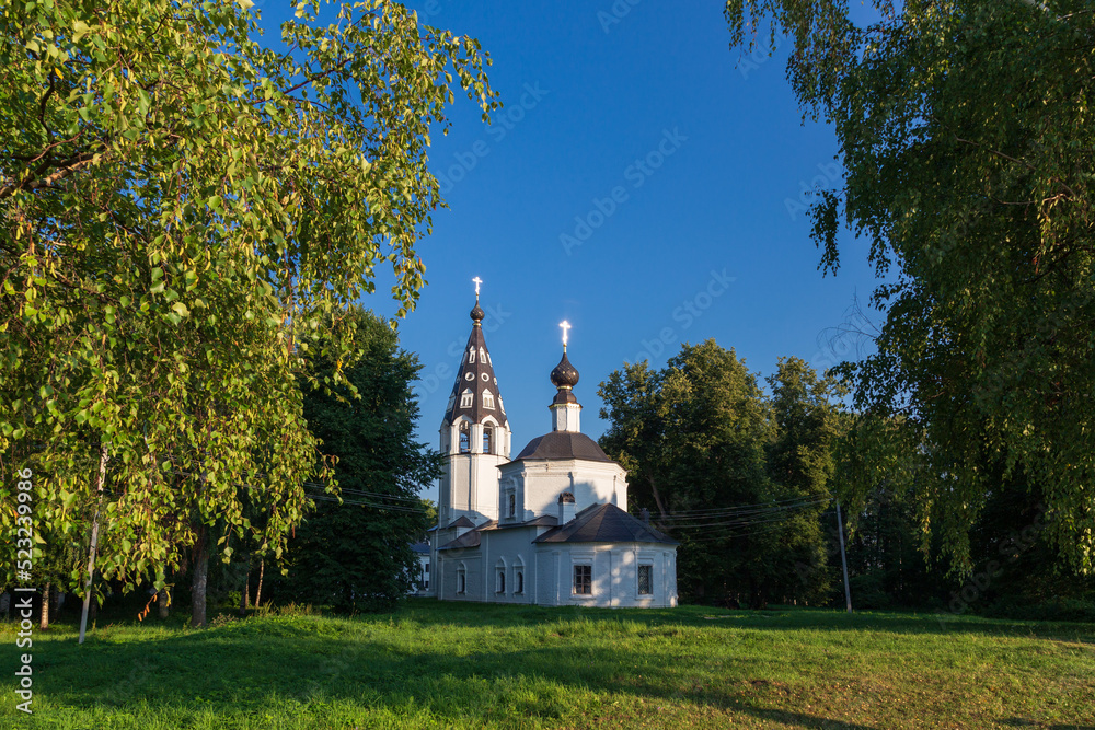 Russian Orthodox church amond big trees framed with birch foliage against clear sky, Plyos, Russia