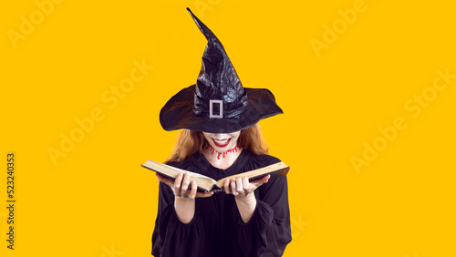 Woman in Halloween costume looking through book of spells. Cunning evil witch with bloody neck cut and creepy happy smile hides face under hat and chooses most terrible curse from witchcraft manual