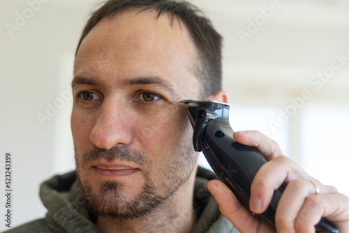 Close up portrait of a handsome shirtless man shaving beard with an electric razor