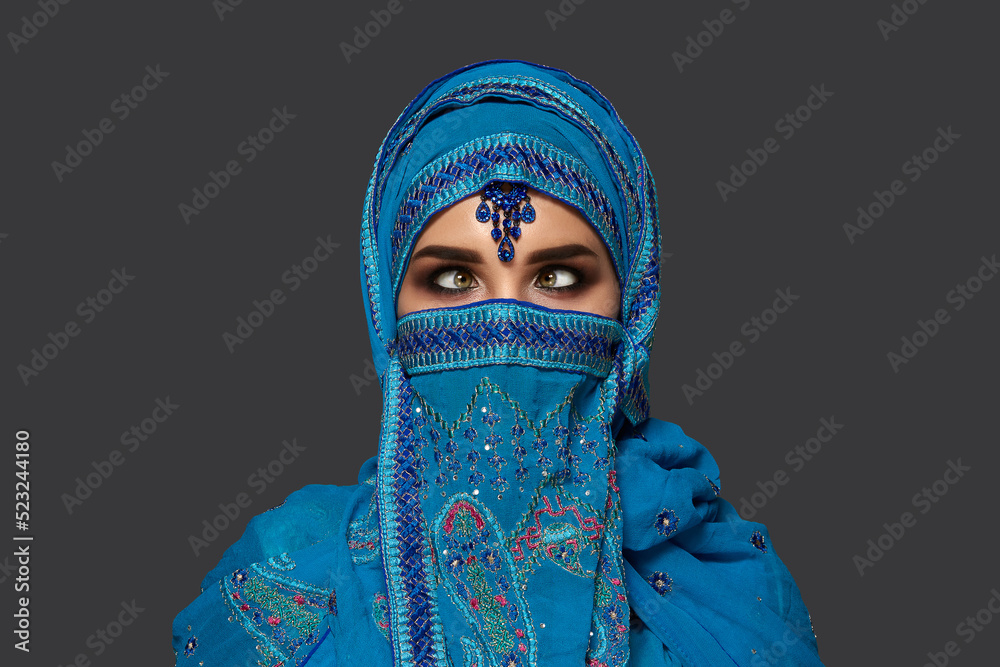 Studio shot of a young beautiful woman wearing the blue hijab decorated with sequins and jewelry. Arabic style.