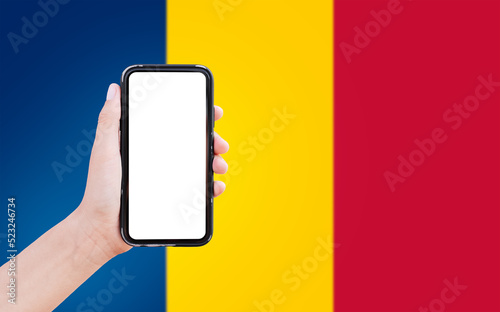 Close-up of male hand holding smartphone with blank on screen, on background of blurred flag of Chad.