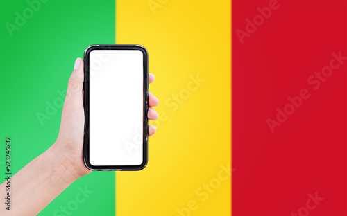 Close-up of male hand holding smartphone with blank on screen, on background of blurred flag of Mali.