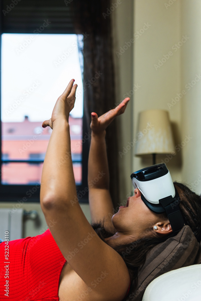 Woman lying in bed with virtual reality goggles on trying to protect herself from something that scares her. Vertical image of young girl in her room trying out augmented reality in three dimensions. Woman lying in bed with virtual reality goggles on trying to protect herself from something that scares her. Vertical image of young girl in her room trying out augmented reality in three dimensions.