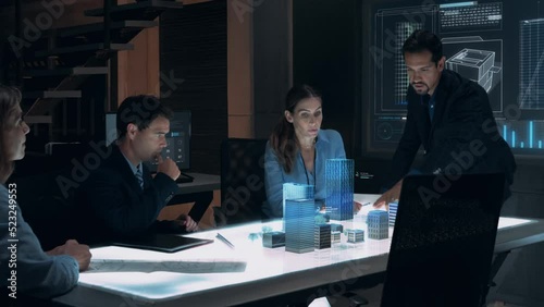 Businessman in Suit presenting Architecture Project to Colleagues and Partners sitting around Futuristic Table with Holographic Modern Augmented Reality Technology.