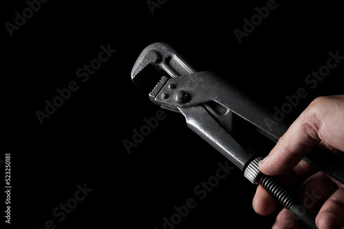 Old gas wrench in hand on a black background