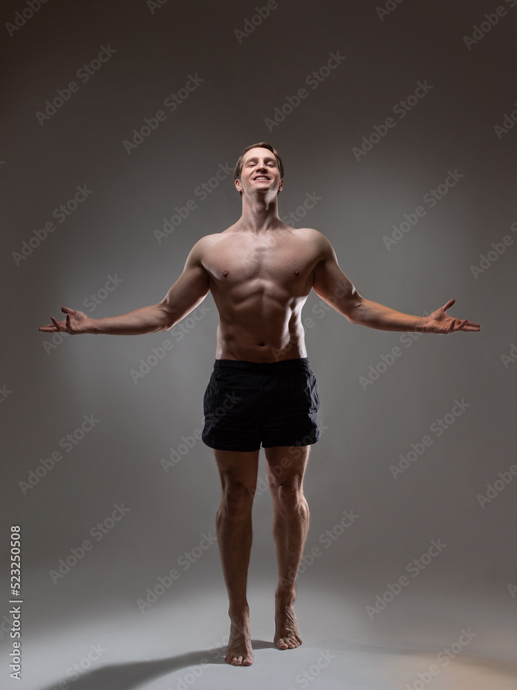 Muscular man in an artistic pose, portrait on a gray background. The guy is an athlete with spectacular muscles posing with his arms outstretched Muscular man in an artistic pose, portrait on a gray background. The guy is an athlete with spectacular muscles posing with his arms outstretched