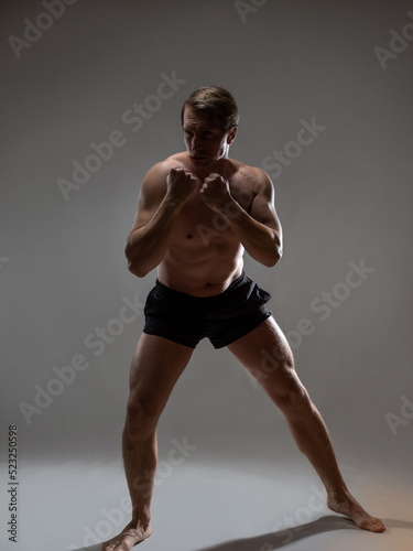 Muscular man in an artistic pose  portrait on a gray background. The guy is an athlete in a wrestling pose. A muscular bodybuilder strains his fists