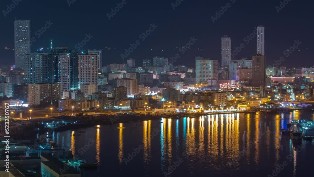 Cityscape of Ajman aerial view from rooftop at night timelapse with reflection of water in lake. Illuminated towers on a waterfront in the United Arab Emirates. Cityscape of Ajman aerial view from rooftop at night timelapse with reflection of water in lake. Illuminated towers on a waterfront in the United Arab Emirates.