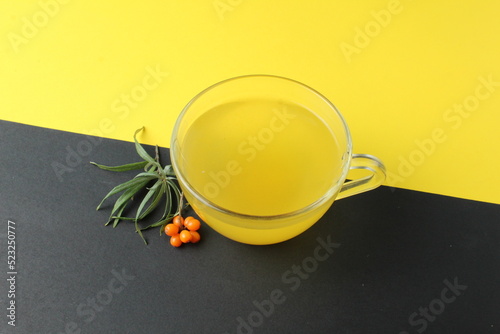 sea buckthorn tea drink on black yellow background. Sea buckthorn juice glass cup next to a spout of sea buckthorn leaves orange berries on a black and yellow background. creative photography.  photo