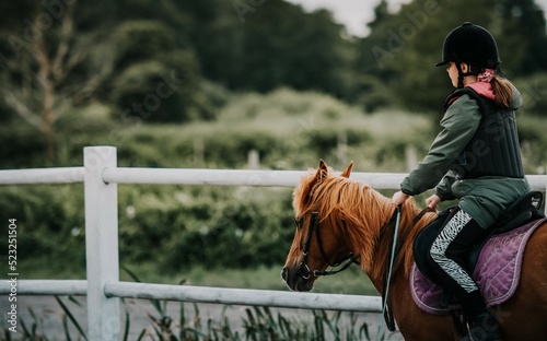 Dziewczynka jeździ konno w szkółce jeździeckiej. Obóz konny, ćwiczenia w siodle na padoku
