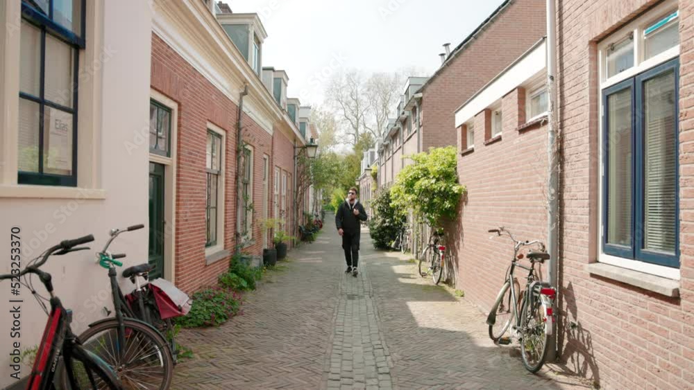 Mature stylish man total-black with bag walking towards camera through streets in Europe on a sunny day. Tourist black jacket with backpack walking on cosy Amsterdam street in fall, spring, summer Mature stylish man total-black with bag walking towards camera through streets in Europe on a sunny day. Tourist black jacket with backpack walking on cosy Amsterdam street in fall, spring, summer