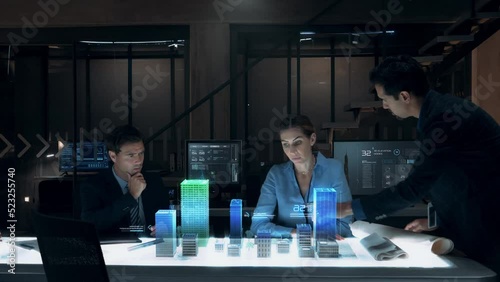 Businessman in Suit presenting Architecture Project to Colleagues and Partners sitting around Futuristic Table with Holographic Modern Augmented Reality Technology. 3D Model of City. Augmented Reality