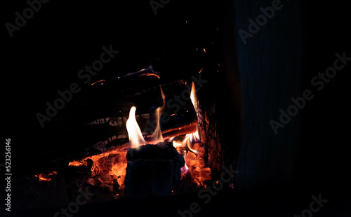 Wood in the fireplace. Burning firewood and fire flames on a dark background. Heating the house with a fireplace.