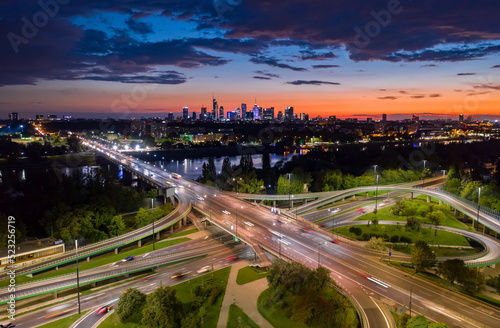 Stunning sunset skyline, aerial Warsaw, Poland. Drone shot of city downtown business center skyscrapers in background. Highway bridge over river and driving cars, amazing cloudscape evening dusk night