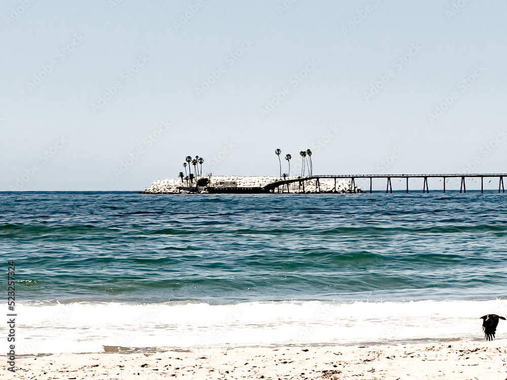 Rincon Island with a blue-green pacific Ocean in the foreground. Waves crashing onto the beach. Rincon Island with a blue-green pacific Ocean in the foreground. Waves crashing onto the beach.
