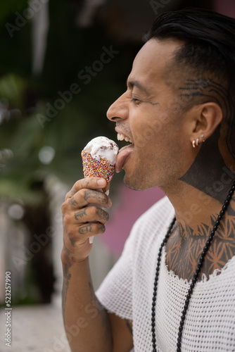 Young handsome mexican tattooed man eating ice cream in a waffle cone.