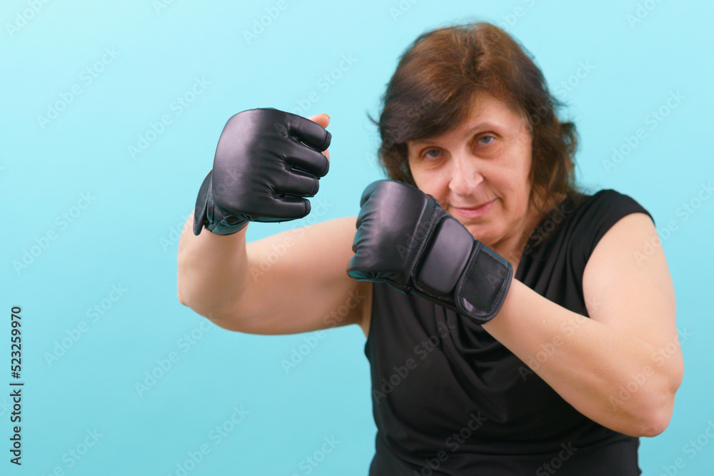 A woman in MMA gloves rising fists up on a blue background. Fighting. Combat. Conflict. Instruction. Box. Artist. Bald. Mixed Martial Arts A woman in MMA gloves rising fists up on a blue background. Fighting. Combat. Conflict. Instruction. Box. Artist. Bald. Mixed Martial Arts