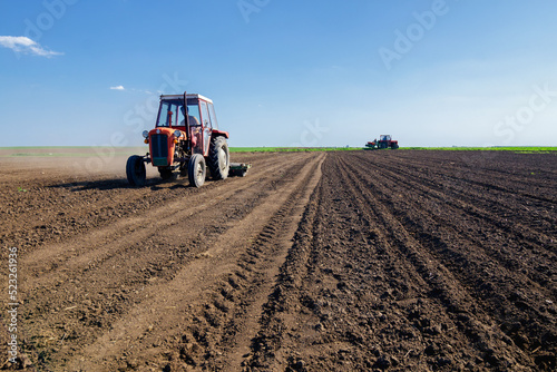 Farmer with tractor sowing on agricultural field on sunny spring day