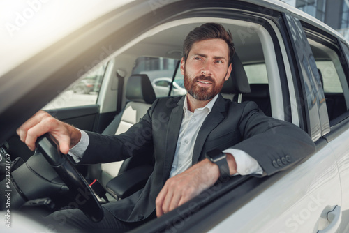 Handsome businessman in grey suit is riding behind steering wheel of car © Kostiantyn