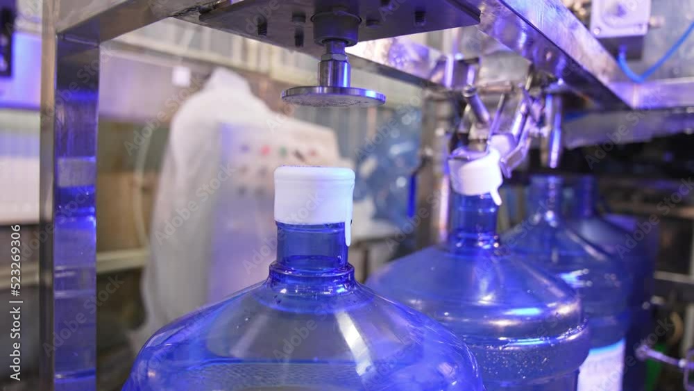 Corking the bottles of fresh clean water. Big flasks filled with water move by the conveyor belt. Mineral water production at factory. Corking the bottles of fresh clean water. Big flasks filled with water move by the conveyor belt. Mineral water production at factory.