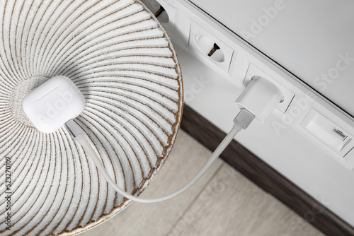 Modern wireless earphones charging from electric socket indoors, above view